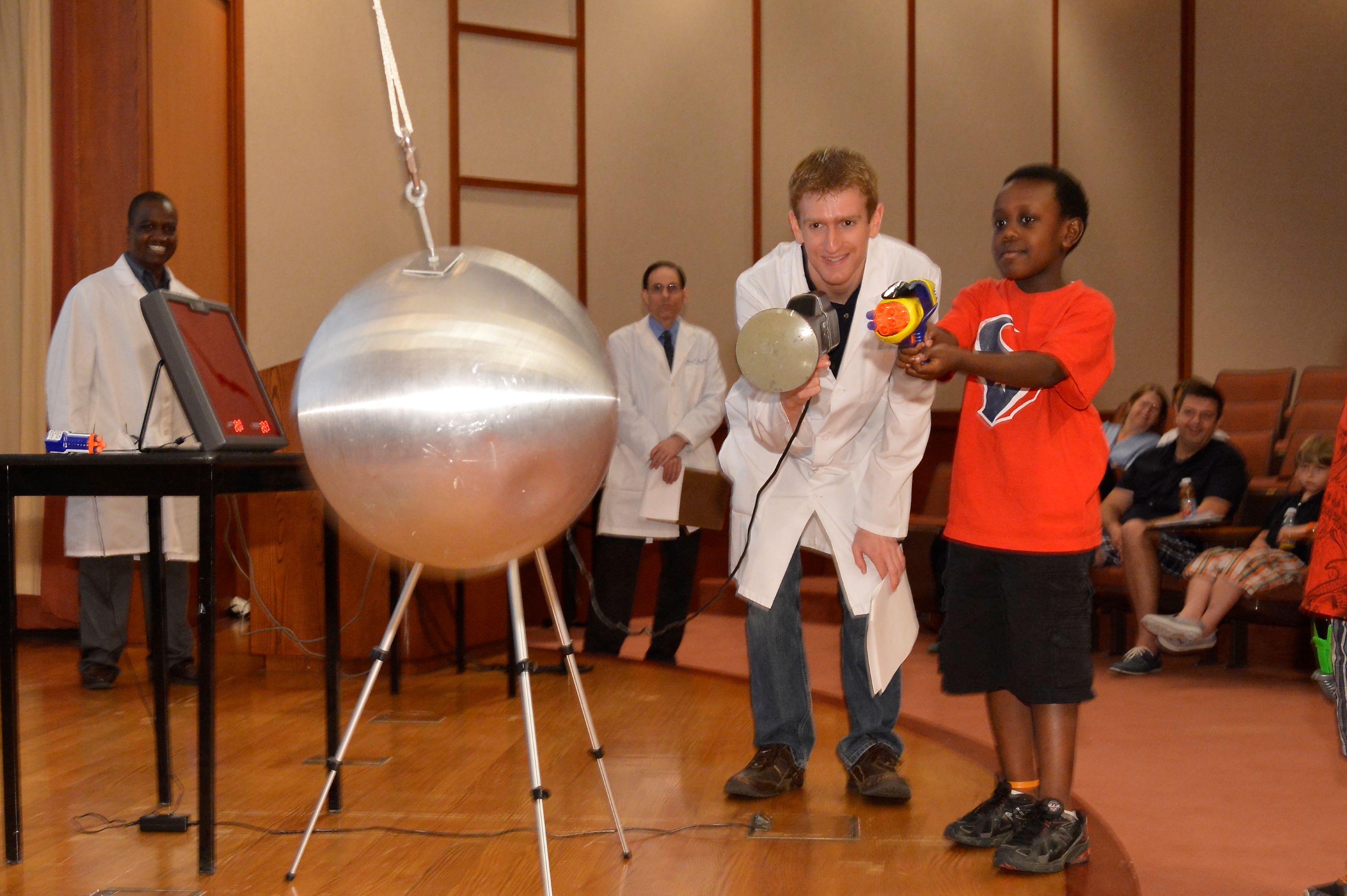 At the Science of Radar show, a child shoots Nerf bullets at a swinging pendulum while a scientist measures the speed of each.